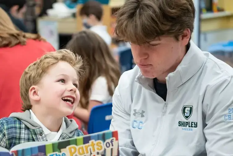 Upper school student reading to lower school student in class